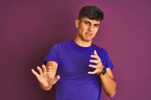 若いインド人男性のTシャツを着て隔離された紫色の背景に立って嫌悪感の反応のために嫌悪感の表情を 不満と恐ろしい嫌な顔をしてうんざりした 手を上げてどんなコンセプトでも — ストック写真
