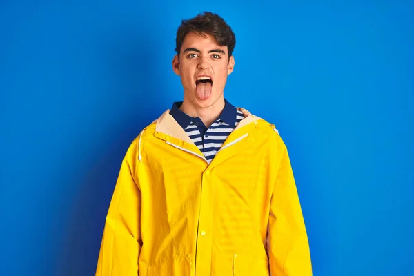 独立した背景に黄色のレインコートを着た10代の漁師の少年が面白い表情で幸せ舌を突き出しています 感情概念 — ストック写真
