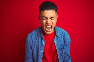 Kotlu tişört giyen genç Brezilyalı adam izole edilmiş kırmızı arka planda ayakta duruyor ve başarı için çılgın ve çılgın bir kutlama yapıyor kollarını kaldırmış ve gözlerini kapamış heyecanla bağırıyor. Kazanan konsept