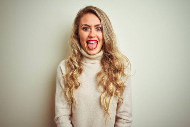 Güzel bir kadın, izole edilmiş beyaz arka plan üzerine balıkçı yaka kazak giyip komik bir ifadeyle dilini dışarı çıkaran güzel bir kadın. Duygu kavramı.