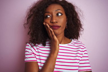 Genç Afro-Amerikalı kadın çizgili tişört giyip izole edilmiş pembe arka plan üzerinde duruyor. Kollarını kavuşturup depresyondan sıkılmış ve yorgun görünüyor..