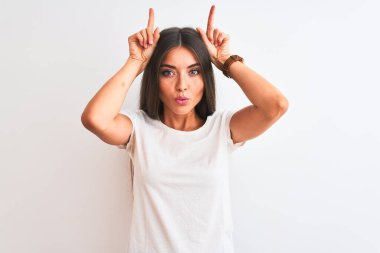 Genç, güzel bir kadın, izole edilmiş beyaz arka planda dikilmiş tişört giyiyordu. Boğanın boynuzları gibi parmağıyla komik jestler yapıyordu.