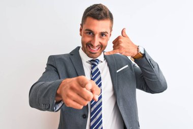 Young handsome business man wearing suit and tie over isolated background smiling doing talking on the telephone gesture and pointing to you. Call me.