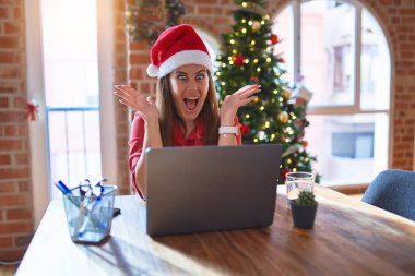 Noel 'de dizüstü bilgisayarla çalışan güzel bir kadın Noel Baba şapkası takıyor çılgın kutlamalar yapıyor ve kollarını kaldırmış ve gözleri açık bir şekilde heyecanla haykırıyor. Kazanan konsept