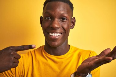 Siyah tişörtlü Afro-Amerikan bir adam izole edilmiş sarı arka planda duruyor.