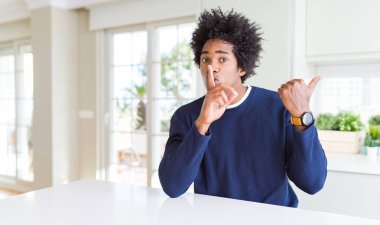 Rahat bir süveter giyen Afro-Amerikan genç adam evde oturmuş, parmakları dudaklarını yana doğru gösteren parmaklarıyla sessiz olmak istiyor. Sessizlik ve gizli konsept.