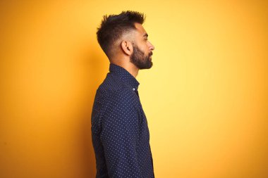 Genç, yakışıklı Hintli işadamı, izole edilmiş sarı arka planda gömlek giyiyor. Yan tarafa bakıyor, rahat poz veriyor, kendine güvenen bir gülümsemesi var..