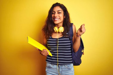 Korunmuş sarı arka planda kulaklık takan öğrenci kadın gururla bağırıyor ve zaferi ve başarıyı kutluyor.