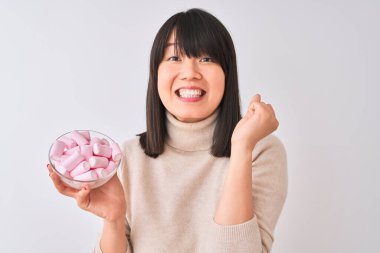 Güzel Çinli kadın, izole edilmiş beyaz arka planda elinde şekerlemelerle gururla bağırıyor ve zaferi ve başarıyı kutluyor. Çok heyecanlı, coşkulu bir duygu.