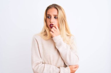 Balıkçı yaka kazak giyen genç ve güzel bir kadın izole edilmiş beyaz arka plan üzerinde duruyor. Elleri ağız ısıran tırnaklarla stresli ve gergin görünüyor. Endişe sorunu.