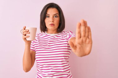 Genç güzel kadın açık el ile izole pembe arka plan üzerinde ayakta kahve içme fincan ciddi ve emin ifade ile stop işareti yapıyor, savunma jest