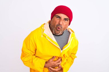 Orta yaşlı yağmurluk giyen ve yünlü şapka takan bir adam midesi bulanan, acı veren bir hastalıktan dolayı el üstünde duran izole edilmiş beyaz bir arka plan. Ache kavramı.