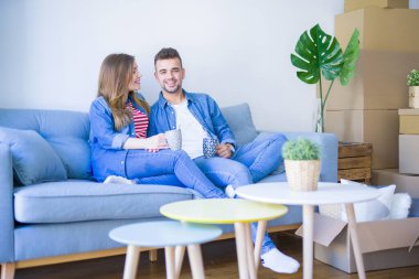 Genç çift etrafında karton kutular ile yeni bir ev kanepede oturan kahve bir fincan içme rahatlatıcı, çok mutlu yeni bir daireye hareket
