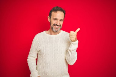 Yakışıklı, orta yaşlı, gri saçlı, izole edilmiş kırmızı arka planı olan, yüzünde kocaman bir gülümseme olan, elini kaldırıp kameraya bakan bir adam..