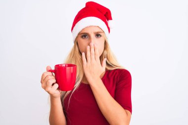 Noel Baba şapkası takan güzel bir kadın izole edilmiş beyaz arka planda kahve içiyor. Ağzı kapalı, utançtan ağzı açık, korkunun dışa vurumu, sessizlikten korkması, gizli konsept.