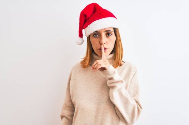 Güzel kızıl saçlı kadın, izole edilmiş arka planda noel şapkası takıyor ve sessiz olmak istiyor. Sessizlik ve gizli konsept.