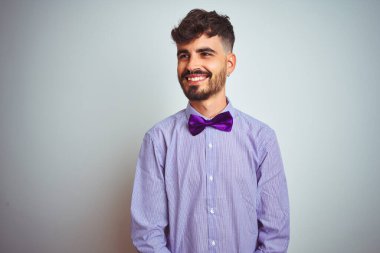 Mor gömlekli ve papyonlu genç bir adam izole edilmiş beyaz arka planda yüzünde gülümseme, doğal bir ifade ile yan yana bakıyor. Kendinden emin gülen.