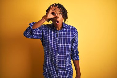 Rastgele gömlek giyen, sarı arka planda dikilen afro saçlı adam şaşırmış yüz ifadesiyle şaşırmış, parmaklarından bakan bir hareket yapıyor. İnançsız ifade.