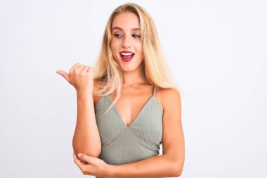 Yeşil tişört giyen genç ve güzel bir kadın izole edilmiş beyaz arka planda durup gülümsüyor ve başparmağıyla yan tarafa bakıyor..