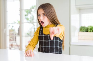 Evde rahat sarı kazak giyen genç güzel sarışın çocuk kız memnun ve kamera için sinirli, öfkeli ve öfkeli