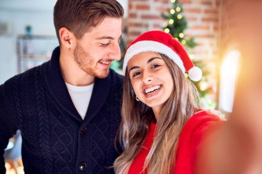 Mutlu ve kendinden emin gülümseyen genç bir çift. Evdeki Noel ağacının etrafında kamerayla selfie çekmek.