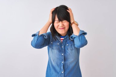 İzole edilmiş beyaz arka plan üzerine kot gömlek giyen genç, güzel Çinli kadın acı ve migren yüzünden çaresiz ve stresli bir baş ağrısı çekiyor. Ellerini başının üstüne koy..