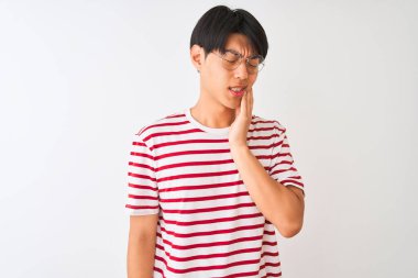 Gözlüklü ve çizgili tişörtlü genç Çinli bir adam izole edilmiş beyaz arka planda durup diş ağrısı ya da diş ağrısı yüzünden acı dolu bir ifadeyle ağıza dokunuyor. Dişçi konsepti.