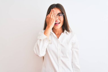 Gözlüklü genç ve güzel bir iş kadını. İzole edilmiş beyaz arka planda duruyor. Bir gözünü eliyle kapatıyor..