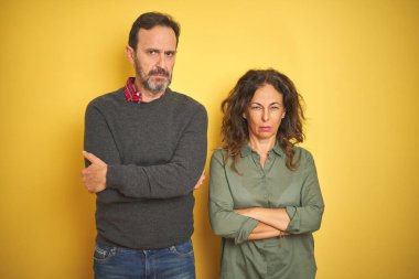Güzel bir orta yaşlı çift izole edilmiş sarı arka plan şüpheci ve gergin kolları çaprazlanmış yüz ifadesini onaylamıyor. Negatif kişi.