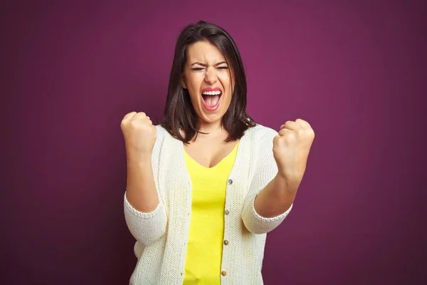 Young beautiful brunette woman a jacket over purple isolated background very happy and excited doing winner gesture with arms raised, smiling and screaming for success. Celebration concept.