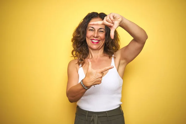 黄色の隔離された背景に立っている巻き毛のある中年のシニア女性は幸せな顔で手や指でフレームを作り笑顔 創造性と写真の概念 — ストック写真