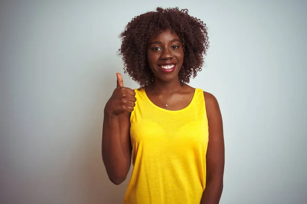 孤立した白い背景に黄色のTシャツを着た若いアフリカのアフロ女性は 手で幸せな親指を上げるジェスチャーをしています 成功を示すカメラを見て表現を承認する — ストック写真