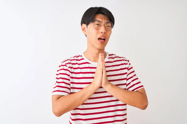 眼鏡と縞模様のTシャツを身に着けている若い中国人男性は 孤立した白い背景を物乞いと手で祈って立って 顔に希望の表現と一緒に非常に感情的かつ心配しました 許しを求める 宗教概念 — ストック写真