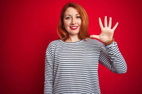 若いですRedhead女性身に着けていますStrapesネイビーシャツ上に立って赤い隔離された背景を示すと指番号5と指摘しながら 自信と幸せ — ストック写真