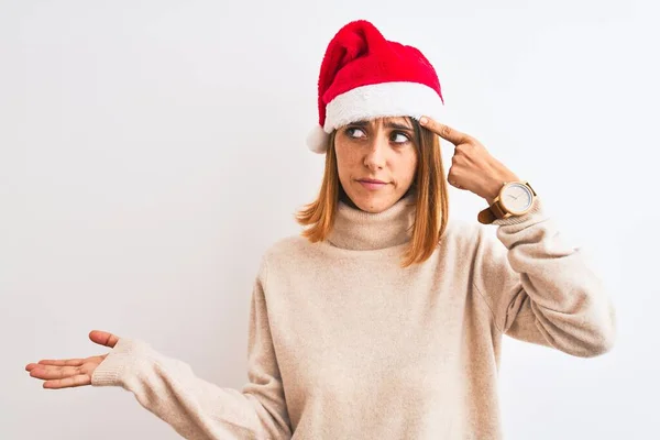 孤立した背景の上にクリスマスの帽子を身に着けている美しい赤毛の女性は混乱し コピースペースを示し 額に指を指すオープンヤシに悩まされました 考えてみて — ストック写真