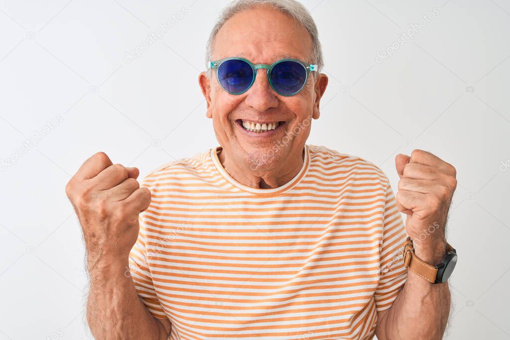 Senior grey-haired man wearing striped t-shirt and sunglasses over isolated white background celebrating surprised and amazed for success with arms raised and open eyes. Winner concept.
