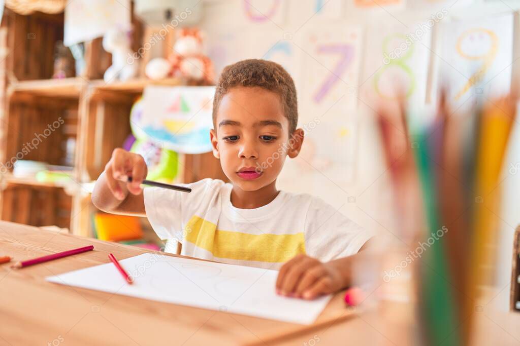 Beautiful african american toddler sitting drawing using paper and pencils on desk at kindergarten