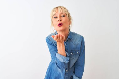 Sıradan bir kot gömlek giyen orta yaşlı bir kadın izole edilmiş beyaz arka planda dikilip kameraya bakarak havada öpücükler savuruyor. Güzel ve seksi. Aşk ifadesi.