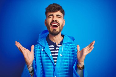 İzole edilmiş mavi arka planda duran genç ve yakışıklı bir adam başarının çılgınlığını kollarını kaldırmış ve gözlerini kapatmış heyecanla haykırarak kutluyor. Kazanan konsept