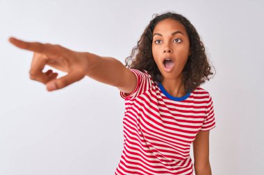 Kırmızı çizgili tişört giyen genç Brezilyalı bir kadın izole edilmiş beyaz arka planda duruyor. Parmakları önde, ağzı açık ve şaşırmış bir şekilde işaret ediyor.