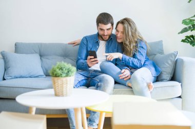 Yeni bir eve hareket akıllı telefon kullanarak kanepede oturan aşk sarılma genç çift