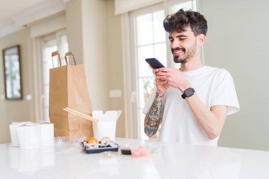 Genç adam alarak fotoğraf ile Smartphone arasında Suşi Asya gıda itibaren almak uzak Delivery