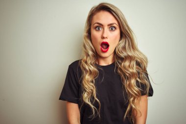 Siyah tişört giyen genç ve güzel bir kadın. İzole edilmiş beyaz arka plan üzerinde duruyor. Şaşırmış ve korkmuş bir ifade, korku ve heyecanlı bir yüz ifadesi var..