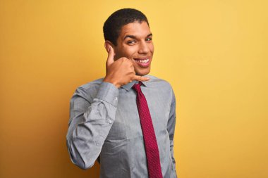 Genç yakışıklı Arap işadamı gömlek ve kravat takıp izole edilmiş sarı arka planda gülümsüyor telefonla el ve parmaklarıyla telefonla konuşuyor gibi yapıyor. İletişim kavramları.