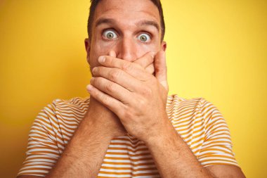 Sarı izole arka plan üzerine gündelik tişört giyen genç yakışıklı bir adam yanlışlıkla ağızlarını kapatıyor. Gizli konsept.