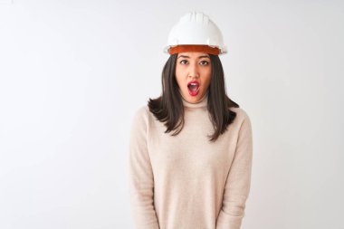 İzole edilmiş beyaz arka plan üzerinde güvenlik kaskı takan genç Çinli mimar kadın şaşkınlık, korku ve şaşkınlık dolu bir ifadeyle ürkmüş ve şok olmuştu..