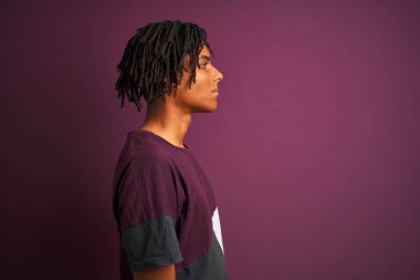 Rastgele tişörtler giyen Afro bir adam. İzole edilmiş mor arka plan üzerinde duruyor. Yan tarafa bakıyor, rahat profil pozu veriyor, kendine güvenen bir gülümsemesi var..