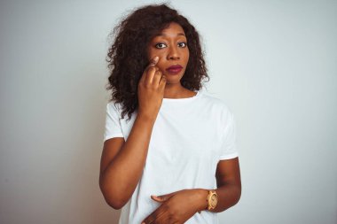 Genç Afro-Amerikalı kadın tişört giyiyor. İzole edilmiş beyaz arka planda dikiliyor. Gözlerine işaret ediyor.