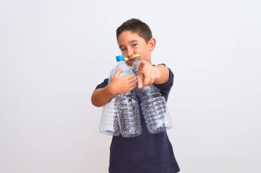 Güzel çocuk, izole edilmiş beyaz arka planda duran plastik şişeleri geri dönüştürüyor. Kamerayı işaret ediyor ve sen, el işareti, ön taraftan pozitif ve kendinden emin bir hareket.