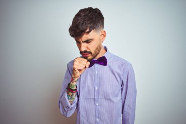 Mor gömlekli ve papyonlu genç adam izole edilmiş beyaz arka planda kendini kötü hissediyor ve soğuk algınlığı veya bronşitin belirtisi olarak öksürüyor. Sağlık hizmetleri kavramı.